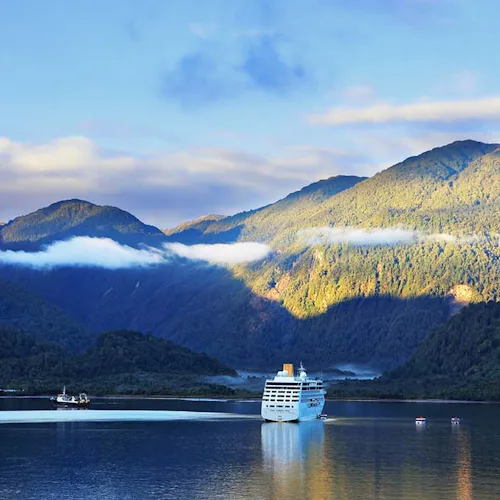 Sunrise in the Chilean fjord. Snow-white tourist ship lit rising sun. On the mountains are thin clouds