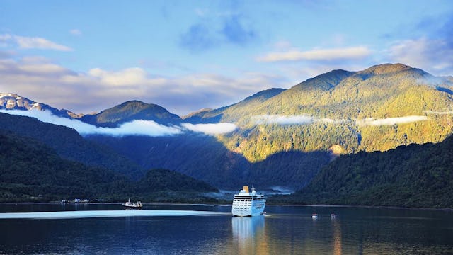 Sunrise in the Chilean fjord. Snow-white tourist ship lit rising sun. On the mountains are thin clouds