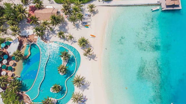 View from a flying drone. Aerial top view of Luxury tropical resort pool with palm trees against the background of the beauty of the sea with coral reefs.