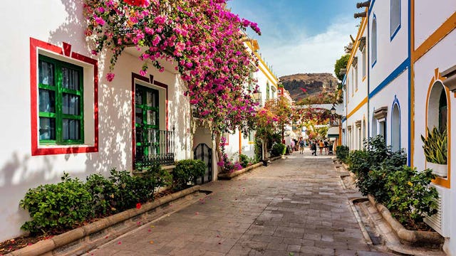 Street with blooming flowers in Puerto de Mogan, Gran Canaria, Spain. Favorite vacation place for tourists and locals on island. Puerto de Mogan with lots of bougainvillea flowers, Canary Island.