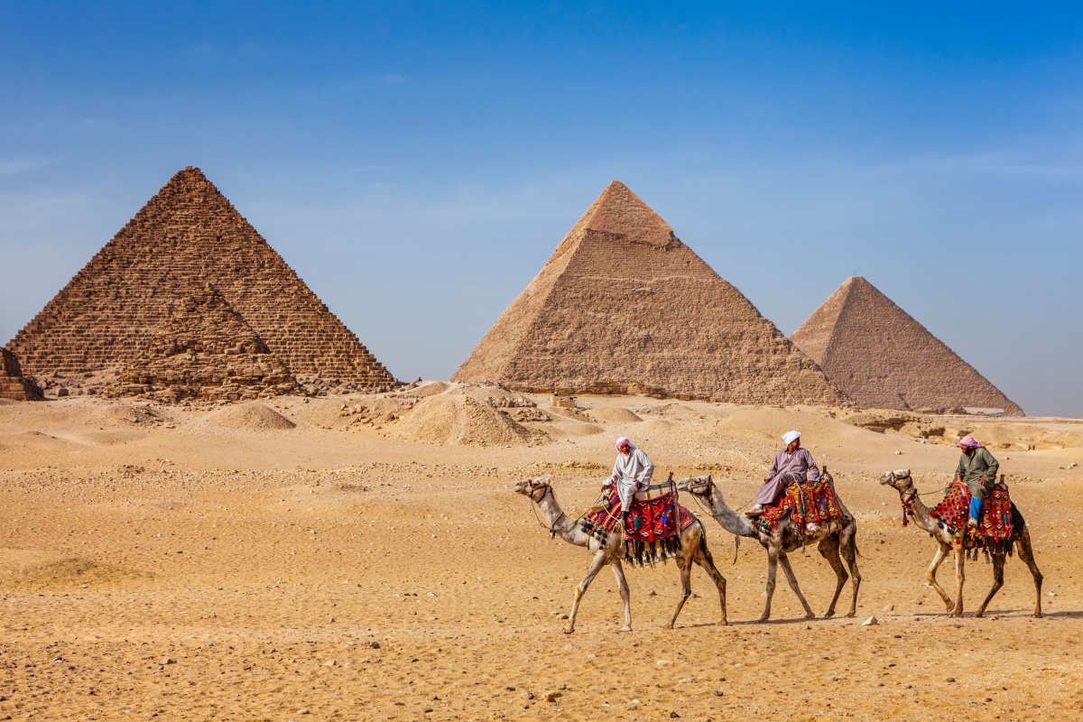Bedouins riding on camels, pyramids on the background, Egypt
