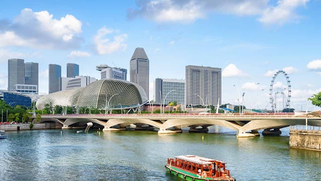Beautiful view of traditional tourist boat sailing along Marina Bay with azure water in Singapore. Amazing modern buildings are visible on blue sky background. Scenic summer cityscape.