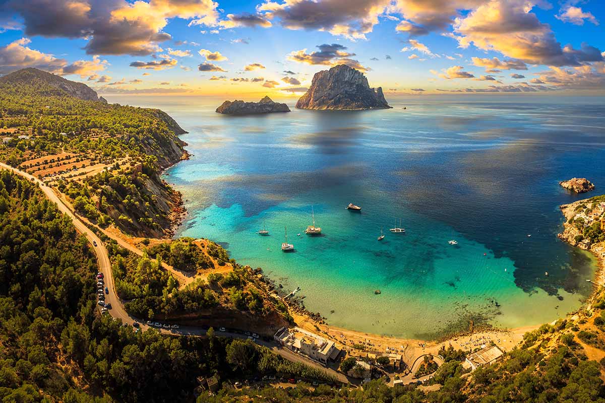 Aerial view of Cala d’Hort beach in Ibiza, featuring the iconic Es Vedrà rock, turquoise waters, and scenic Mediterranean coastline.